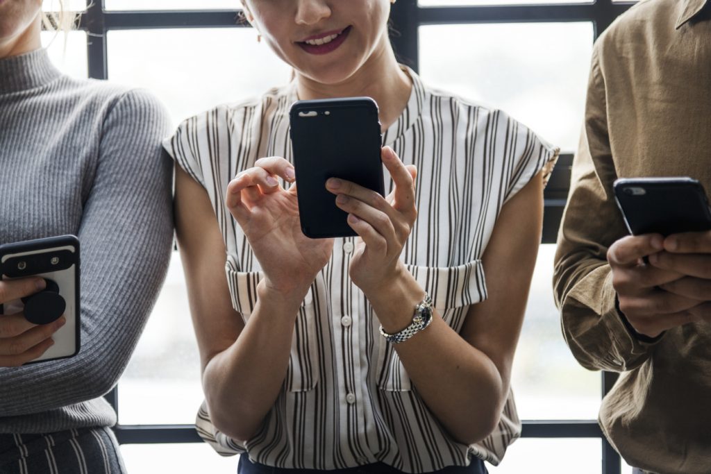 Três pessoas sentadas, uma ao lado das outras, mexendo em smartphones