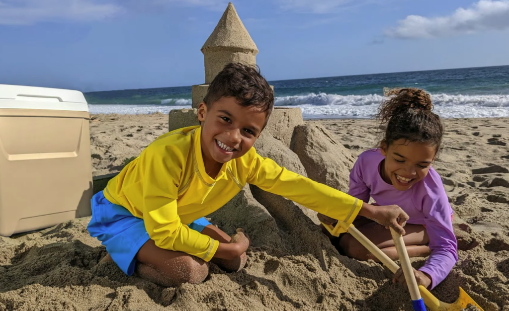 Foto de duas crianças, um menino e uma menina, brincando de castelo de areia na praia: a imagem foi usada durante o Google I/O 2022 para apresentar o recurso de edição de fotos "Magic Eraser" do Pixel 6A