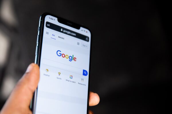 Imagem mostra um smartphone segurado em uma mão, com a tela inicial do Google aberta em seu display