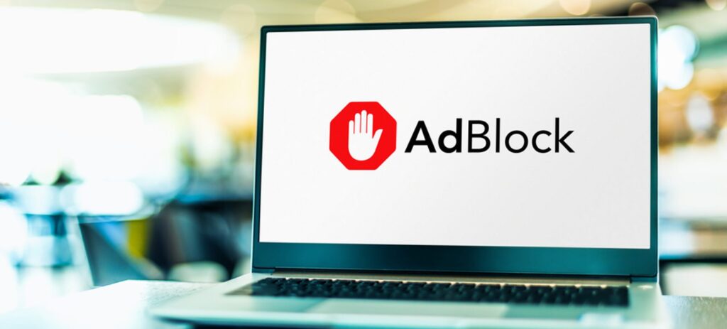 Notebook em cima da mesa exibe, na tela, a ilustração de uma mão fazendo o símbolo de 'pare' com o texto adblock ao lado