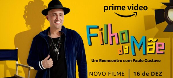 À direita do pôster está o texto "Filho da Mãe, um reencontro com Paulo Gustavo", sobre o filme-documentário do Prime Vídeo. Na imagem, o ator Paulo Gustavo vestido com blazer e chapéu pretos, e a sombra do ator é a silhueta da Dona Hermínia, personagem mais famosa interpretada por ele