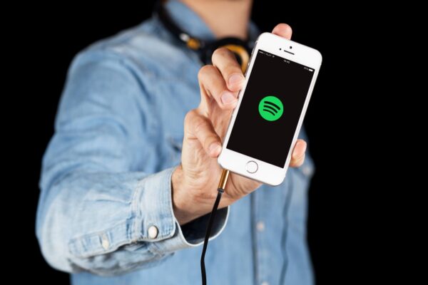 Imagem mostra um homem segurando um smartphone com o aplicativo do Spotify aberto na tela