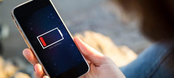 Vista do close-up de uma jovem segurando um smartphone; a tela do aparelho mostra a ilustração de uma bateria fraca