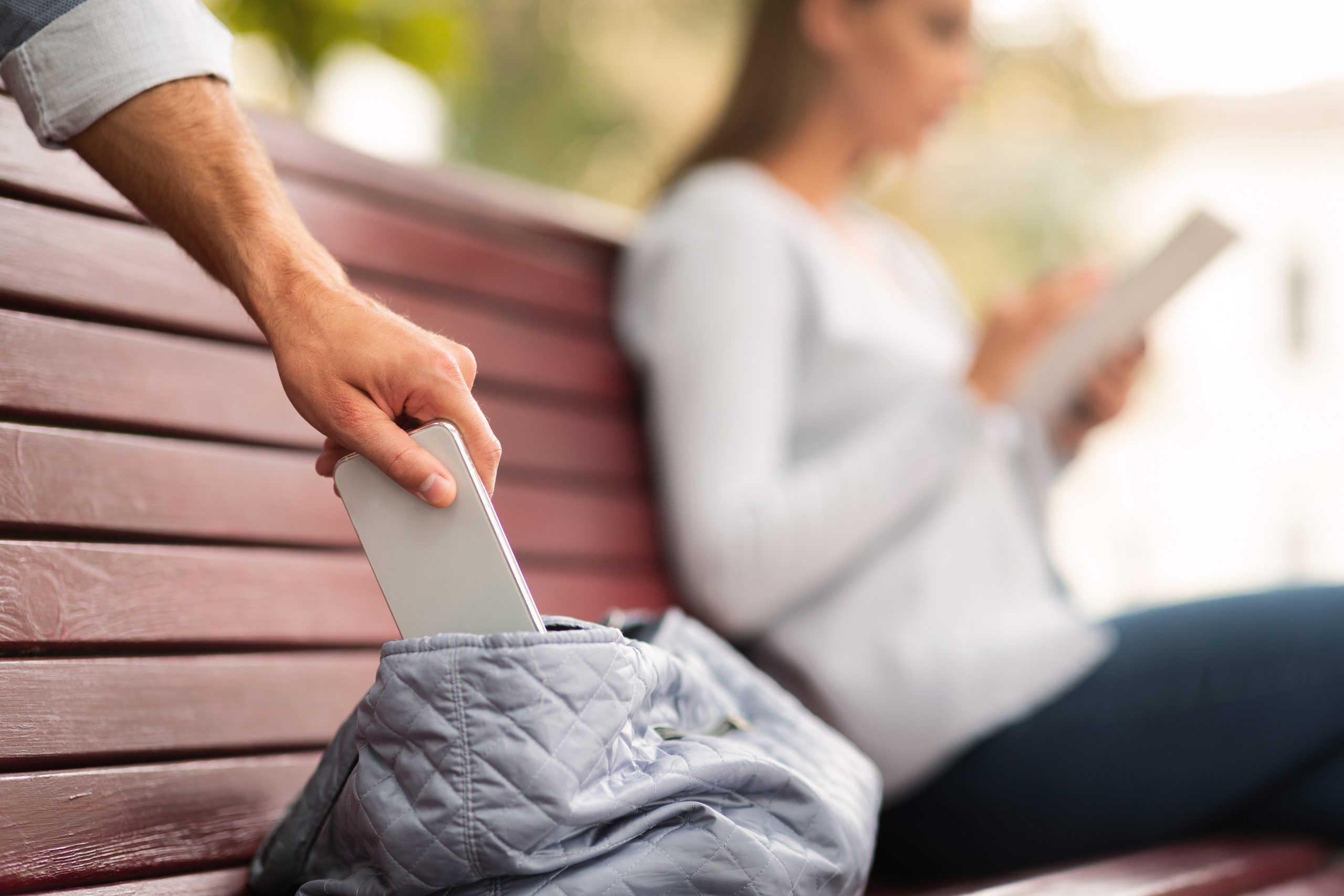 Imagem mostra um ladrão furtando um celular da bolsa de uma mulher distraída