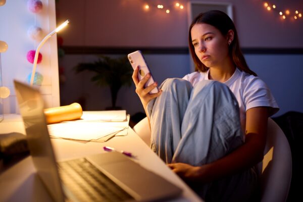 Imagem mostra uma menina adolescente olhando para o celular com o rosto preocupado