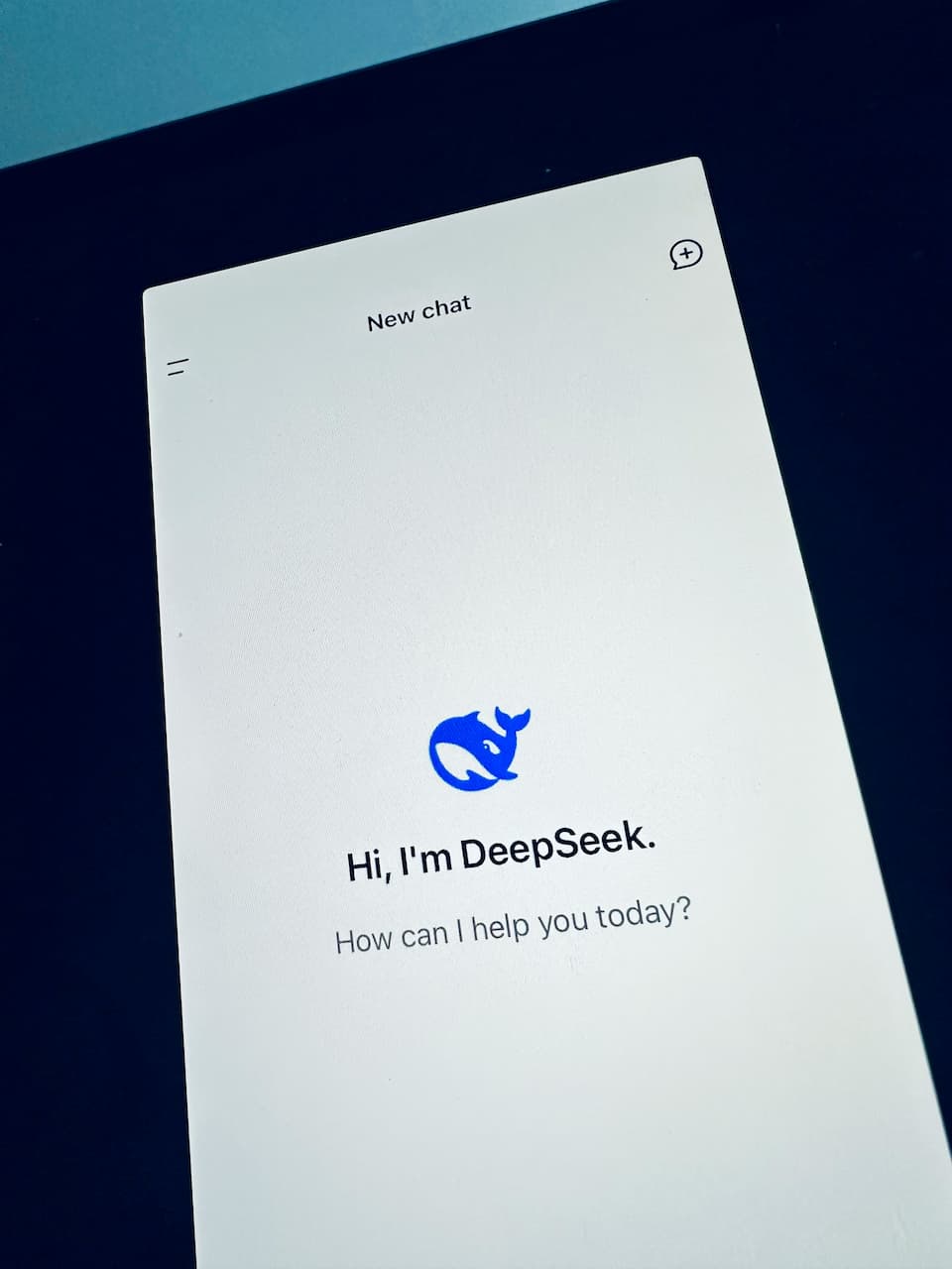 Tela de um dispositivo exibindo a interface do DeepSeek, um chatbot de inteligência artificial. A tela mostra a mensagem de boas-vindas: 'Hi, I'm DeepSeek. How can I help you today?'. O fundo é claro, com um ícone azul representando o DeepSeek no centro.